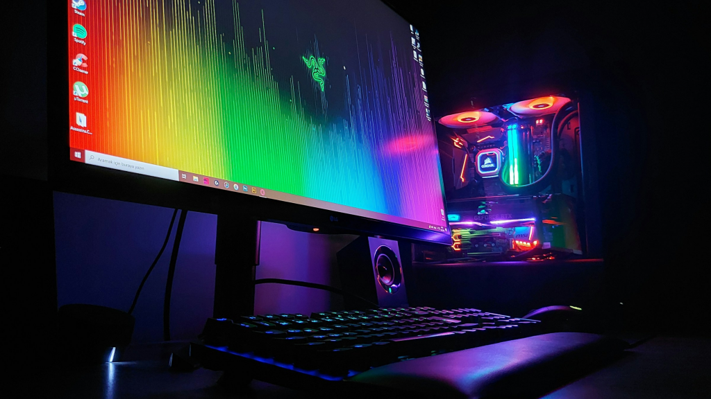imagem mostra um pc gamer, dando ênfase para um monitor colorido, um gabinete com parede transparente e brilhando com luzes rgb