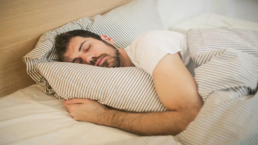 Homem deitado dormindo em uma cama abraçado ao travesseiro