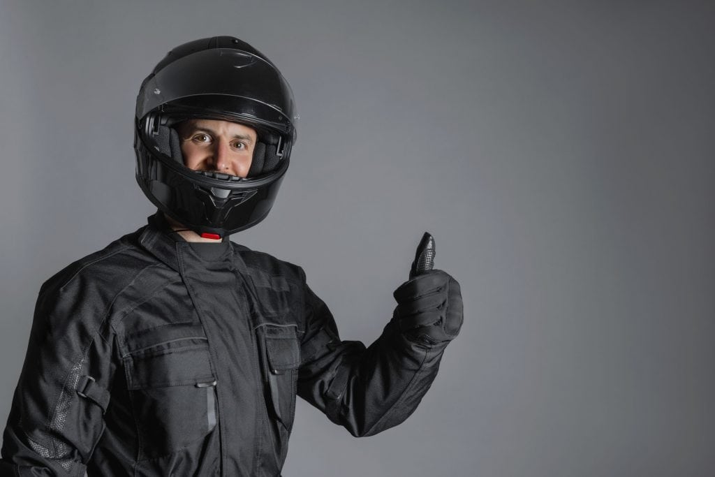 Imagem mostra homem motociclista com capacete de moto fazendo gesto de positivo